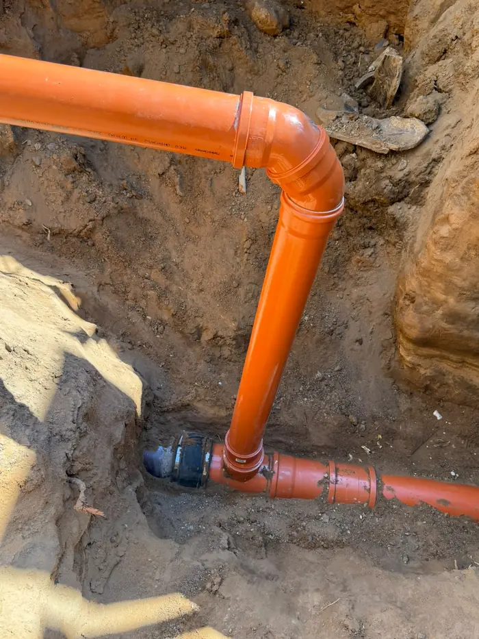 Erneuerte Bruchstelle der Grundleitung: neu verlegtes KG-Rohr mit Bogen und Kupplung in der Baugrube